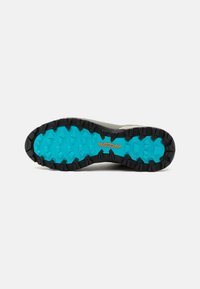 Grijze sport schoen zool met een gestructureerde zwarte buitenkant en een helder turkoois patroon. Bevat hexagonale noppen voor grip en het merklogo.