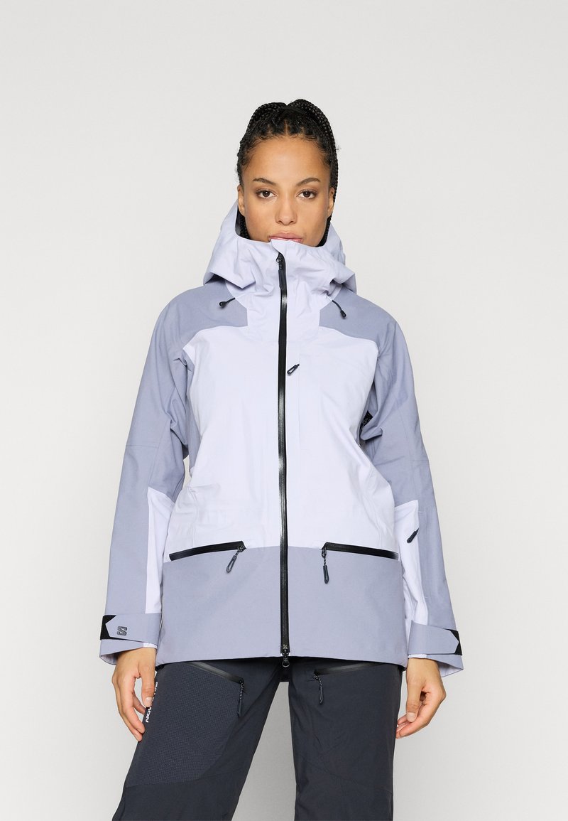 Svetlo siva nepremočljiva jakna s temno sivojimi poudarki. Ima zadrgo na sprednji strani, nastavljivo kapuco in več žepov z zadrgo. Gladek videz.