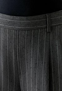 Pantalons en tissu pied-de-poule gris avec de délicates rayures blanches, présentant une ceinture lisse et des détails texturés subtils.