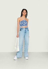 Top crop halter em padrão azul e branco, jeans claros de cintura alta, ténis brancos e uma mala branca com pormenores em tachas.