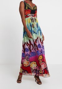 Robe maxi présentant un motif floral avec des couleurs rouge, noir, vert et violet. Design fluide avec un décolleté profond en V et sans manches.