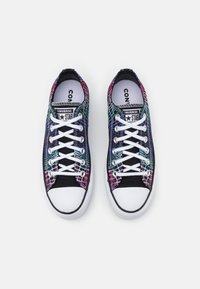 Zapatillas gráficas con un patrón de telaraña multicolor en un upper de tela negra, cordones blancos y una suela de goma blanca con punta redondeada.