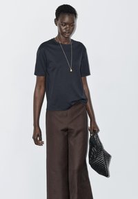 Marineblå t-shirt med korte ærmer, kombineret med brede brune bukser. Holder en sort taske med tekstur. Enkel, afslappet pasform og minimalistisk design.
