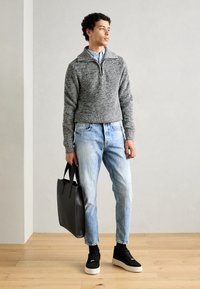Pull en maille gris avec un col zip, chemise bleu clair en dessous, jeans bleu clair, baskets noires et sac fourre-tout noir.