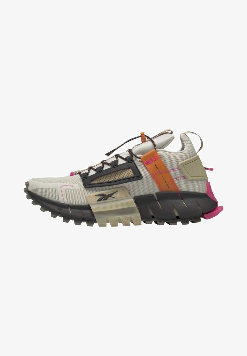 Zapatilla deportiva beige y negra con suela robusta, detalles en naranja y rosa, parte superior de malla y cordones elásticos ajustables con cierre tipo toggle.