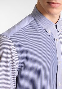 Blauwe en witte gestreepte overhemd met knopen, voorzien van een klassieke kraag, soepel materiaal en een getailleerde pasvorm, met onderscheidende stiksels op de schouder.