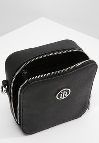 Borsa a tracolla nera con una finitura testurizzata, zip in argento e un logo sulla parte anteriore. Aperta per rivelare un scomparto interno.