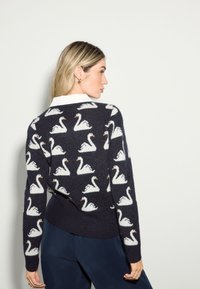 Mörkblå tröja med mönster av vita svanar, gjord av mjukt material med ribbad fåll och muddar; designad med rund halsringning och långa ärmar.