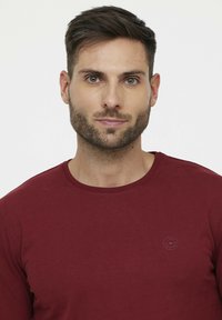 Heren burgundy langemouw t-shirt van zachte katoen. Voorzien van een ronde halslijn en klein rond logo op de linkerkant van de borst. Soepele textuur.