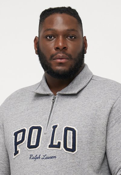 Szürke, cipzáros kapucnis pulóver, magas gallérral és hímzett "PO LO" felirattal tengerészkék és krémszínű kombinációban, puha textúrával és sportos kialakítással.