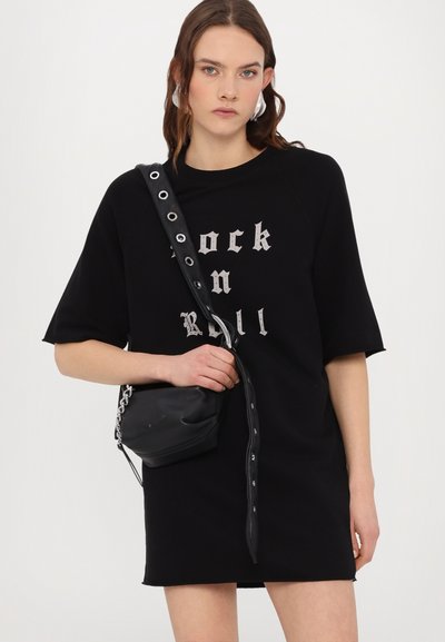 Vestido de algodón negro con un corte holgado, que presenta un estampado gráfico "Rock n Roll" en plata. Combinado con un pequeño bolso negro y acentos plateados.