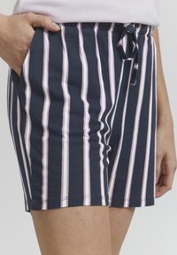 Shorts bleu marine avec des rayures verticales roses et blanches. Dotés d'une taille élastique avec cordon de serrage et de poches latérales. Matière en coton douce.