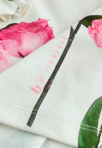 Bloemen katoenen stof met roze rozenprints op een witte achtergrond. Heeft gestikte randen en branding in lichtroze "b by Ted Baker."