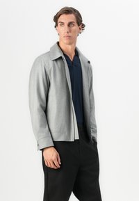 Gray, tailored jacket with a spread collar, front zipper, and long sleeves; paired with a navy polo and black trousers.