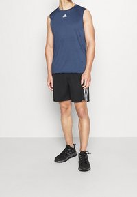 Tílko tmavě modré barvy bez rukávů, černé šortky s bílými pruhy a černé běžecké boty. Jednoduchý design s prodyšnou tkaninou odvádějící vlhkost.