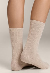 Calze beige a coste realizzate in materiale morbido e testurizzato, dotate di un bordo morbido e una vestibilità aderente alla caviglia, che evidenziano linee verticali.