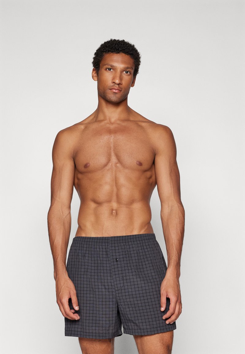 Gray plaid swim shorts feature an elastic waistband and a single button detail. Made from lightweight fabric, designed for comfort.