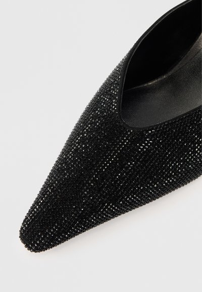 Μαύρο παπούτσι με κοφτή μύτη καλυμμένο με μικρές λαμπερές ρινοστάτες, με μια απλή μαύρη εσωτερική επένδυση και κομψή σιλουέτα.