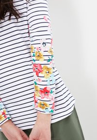 Randig långärmad topp med blommiga detaljer i rött, rosa, gult och blått på ärmarna. Tyget verkar mjukt med en avslappnad passform.