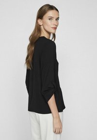 Svart långärmad topp med rullbara ärmar, avslappnad passform och rundad halsringning. Mjuk textur och minimalistisk design, i kombination med vita byxor.