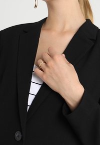 Blazer noir au design structuré, associé à un haut rayé blanc et noir. Une bague en or orne la main, mettant en valeur le détail des accessoires métalliques.