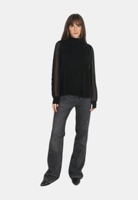Maglione nero con colletto alto e maniche lunghe trasparenti, abbinato a jeans svasati scuri e scarpe nere. Design semplice, senza motivi né accenti.