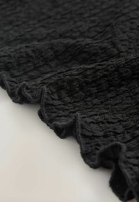 Must tekstureeritud kangas, millel on kootud muster ja volsiline ääris. Materjal tundub kerge ja pehme, sobides ideaalselt kihiliseks kandmiseks või rippumiseks.