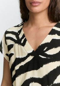 Haut noir et crème à motif v-neck avec des manches courtes, arborant un imprimé zèbre audacieux et une texture de tissu douce.