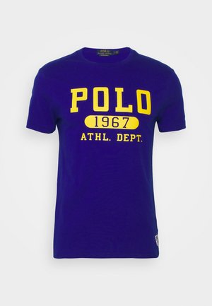 Niebieska koszulka z krótkim rękawem z żółtym napisem „POLO 1967 ATHL. DEPT.” na przodzie i okrągłym dekoltem.