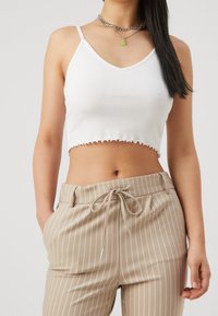 Top court à rayures blanches avec ourlet festonné et bretelles spaghetti, associé à un pantalon taille haute à rayures beiges avec une taille à cordon.