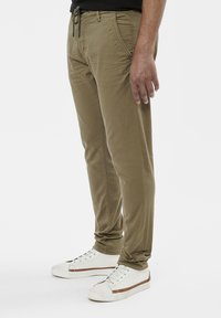 Chino kaki à coupe slim, avec une taille à cordon, des poches latérales et des coutures ton sur ton. Associe à des baskets blanches avec des accents marron.