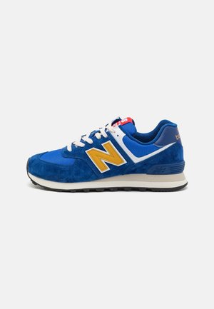 Niebiesko-żółty sneaker New Balance z białymi sznurówkami i podeszwą, pokazany z boku na jednolitym jasnoszarym tle.