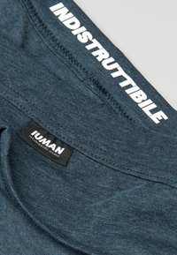 Modré bavlněné spodní prádlo s hladkým povrchem, elastickým pasem s nápisem "INDISTRUTTIBILE" v bílé barvě a černou etiketou s textem "IUMAN."