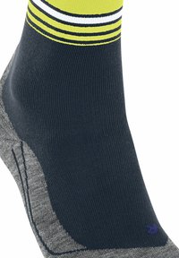 Zbliżenie skarpetki w ciemnoniebieskim kolorze, z szarym piętą oraz jasnoskalowym wykończeniem w żółto-białe paski. Na obszarze kostki widnieje napis "24k".