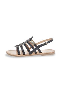 Sandalia negra con tiras, upper texturizado, correa ajustable en el tobillo y suela plana. Presenta un acento en hardware dorado en la tira frontal.