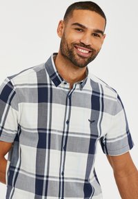 Camisa de cuadros de manga corta en azul, gris y blanco. Presenta un cuello con botones y un logo bordado. Confeccionada en tejido ligero.
