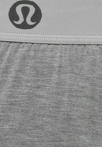 Tela de mezcla de algodón gris con un acabado texturizado, que presenta un logo negro en la cinturilla. El diseño es simple y sin costuras.