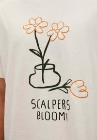 Witte T-shirt met zwart omlijnd vaasje en twee bloemen. De bloemen hebben oranje stiksel, met daaronder "SCALPERS BLOOM!" gedrukt.