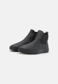 Botas de tobillo de cuero negro con paneles laterales elásticos, punta redondeada y suela de goma contrastante. Textura suave con detalles de diseño mínimos.