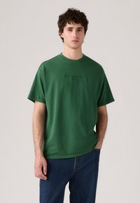 Zelené bavlněné tričko s kulatým výstřihem a krátkými rukávy, na přední straně s embosovanou značkou "Levi's". Nosené s modrými džíny.