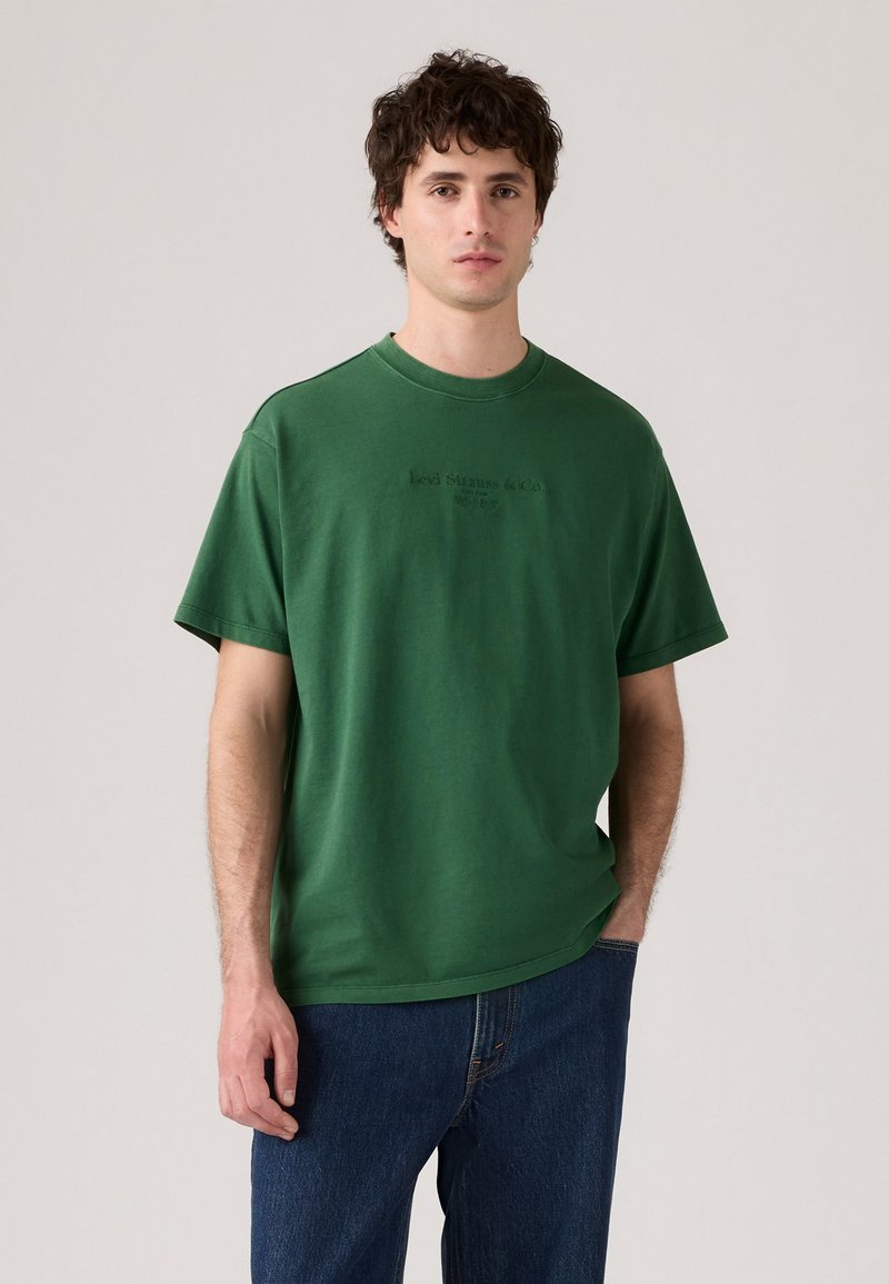 Zelené bavlněné tričko s kulatým výstřihem a krátkými rukávy, na přední straně s embosovanou značkou "Levi's". Nosené s modrými džíny.