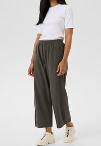 T-shirt blanc à manches courtes associé à un pantalon ample, vert olive, longueur cheville et des baskets de couleur claire. Tenue décontractée.