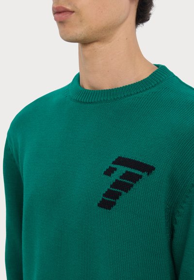 Pull en tricot vert avec un col rond et un design de point d'interrogation pixelisé noir en évidence sur le côté gauche.