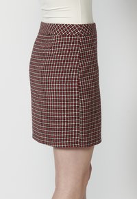 Jupe à carreaux rouge et blanc avec un design ajusté et un tissu texturé. Présente une coupe droite et une taille lisse.