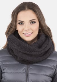 Zwarte gebreide oneindigheidssjaal van dikke garen, met een gestructureerd patroon. gedragen over een grijze gewatteerde jas, biedt warmte.