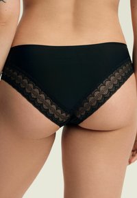 Czarne majtki bikini z gładkiego materiału, ozdobione falistą koronką po bokach. Posiadają miękką fakturę i elastyczny pasek w talii.