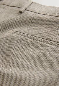 Tissu beige à motif avec un design à carreaux subtil, comprenant une poche arrière à finition nette et une texture lisse.