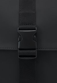 Boucle à dégagement latéral en plastique noir fixant deux extrémités d'une sangle en nylon noir texturée sur une surface sombre et lisse.