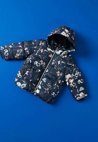 Veste matelassée pour enfants bleu marine avec capuche, motif floral et fermeture éclair à l'avant, posée à plat sur un fond bleu.