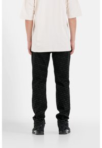 Pantaloni jogger neri con un delicato motivo testurizzato, abbinati a una t-shirt oversize color crema e sneakers nere. Cuciture visibili e vestibilità comoda.